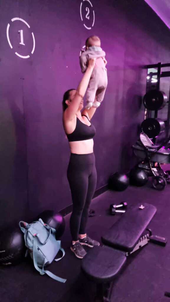 Woman lifting baby up above head in a gym environment